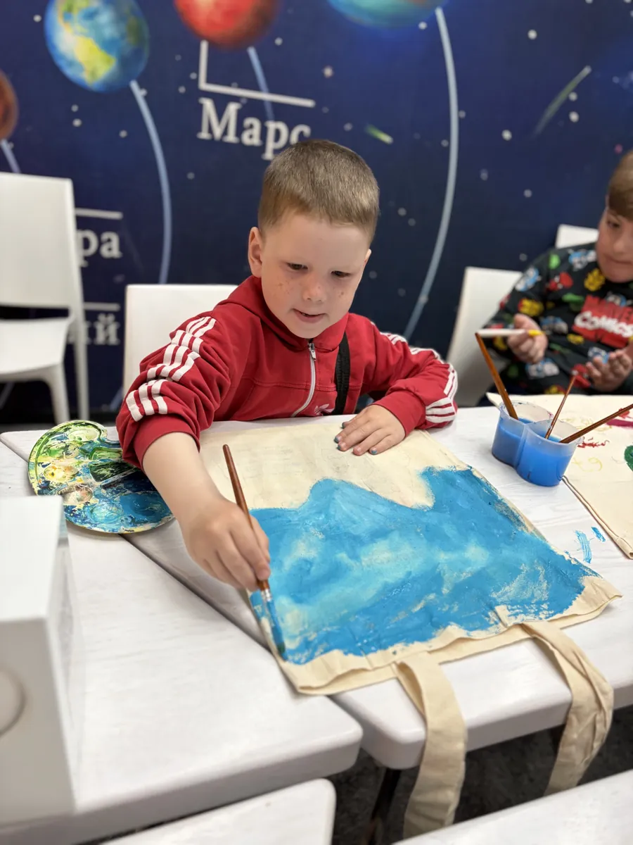 Мальчик расписывает красками холщовую сумку на мастер-классе Магіка